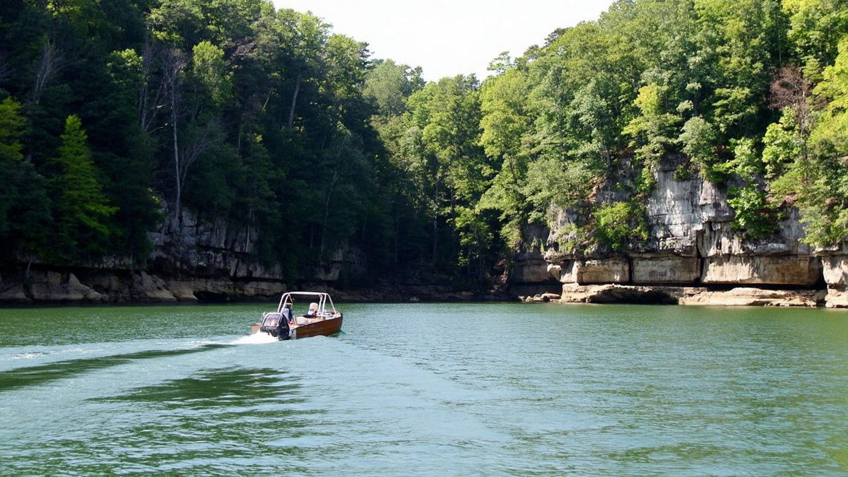 Boat cruising below limestone bluffs on a clear green Ozark lake