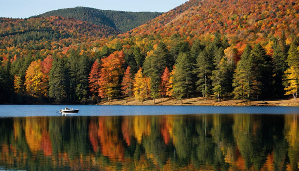 Autumn foliage on wooded hills around a calm lake with a small boat in the distance