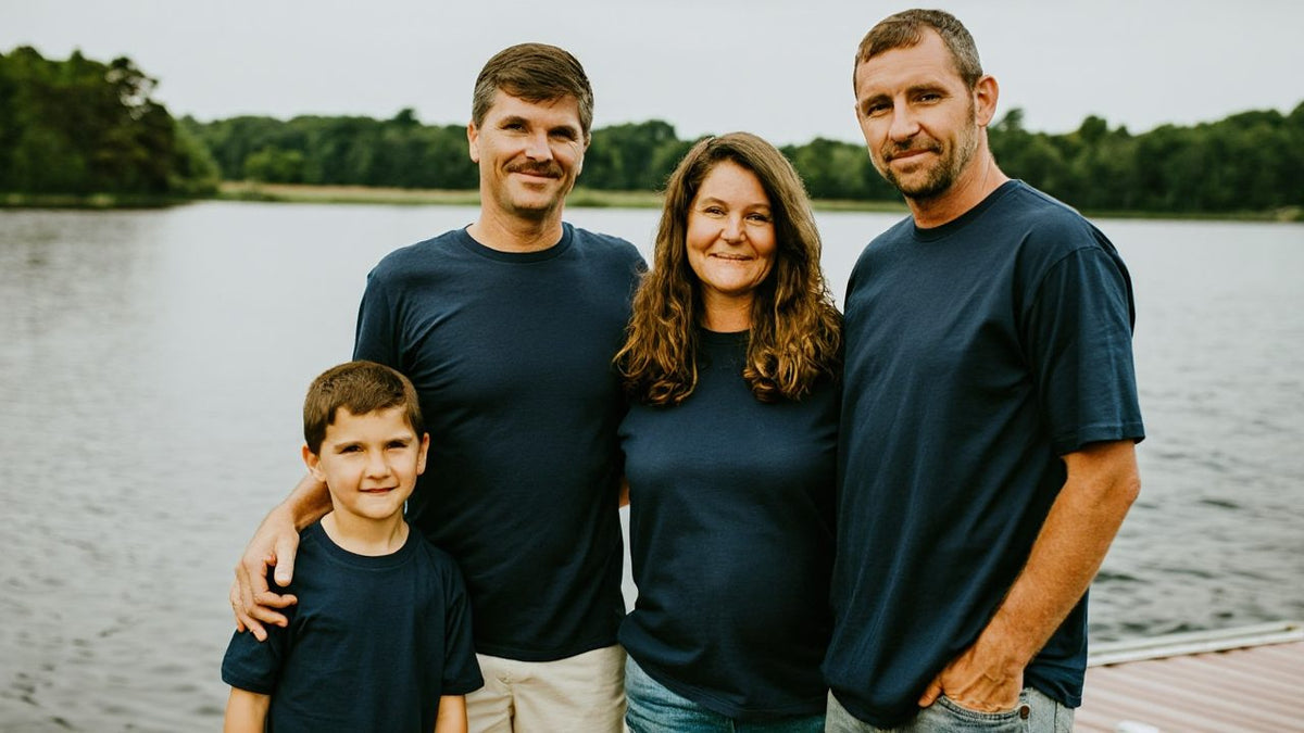 Family of four in matching navy t-shirts standing on a dock by a wooded lake