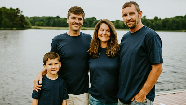 Family of four in matching navy t-shirts standing on a dock by a wooded lake