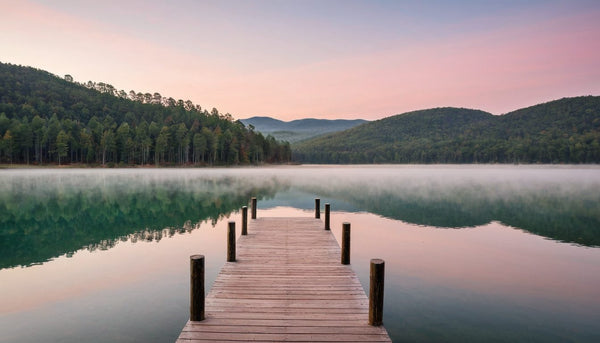 Wooden dock reaching into a calm, misty lake at sunrise with wooded hills beyond