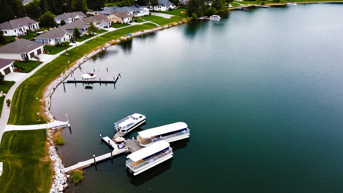 Lake homes along a calm wooded lake with pontoon boats tied up at a dock
